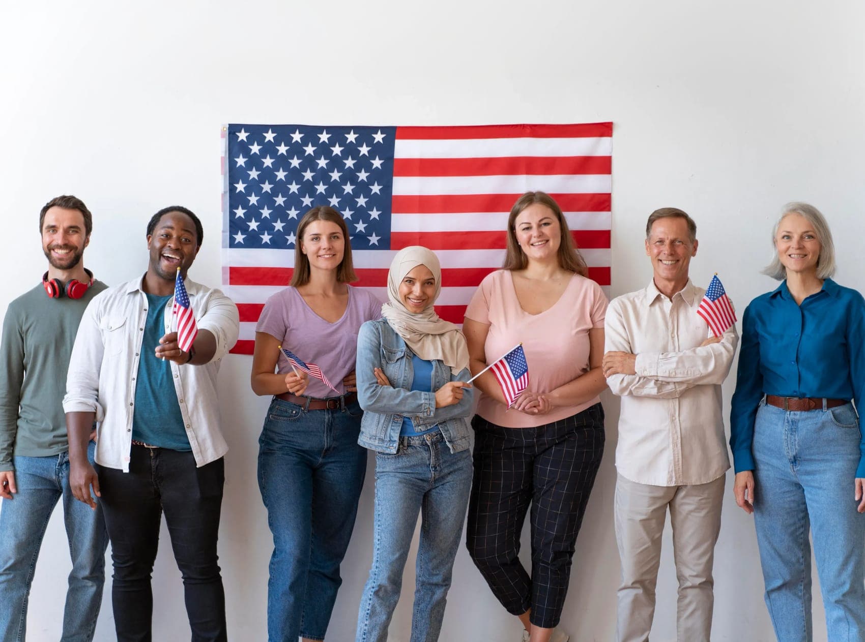 A diverse group of people holding small US flags in front of an American flag