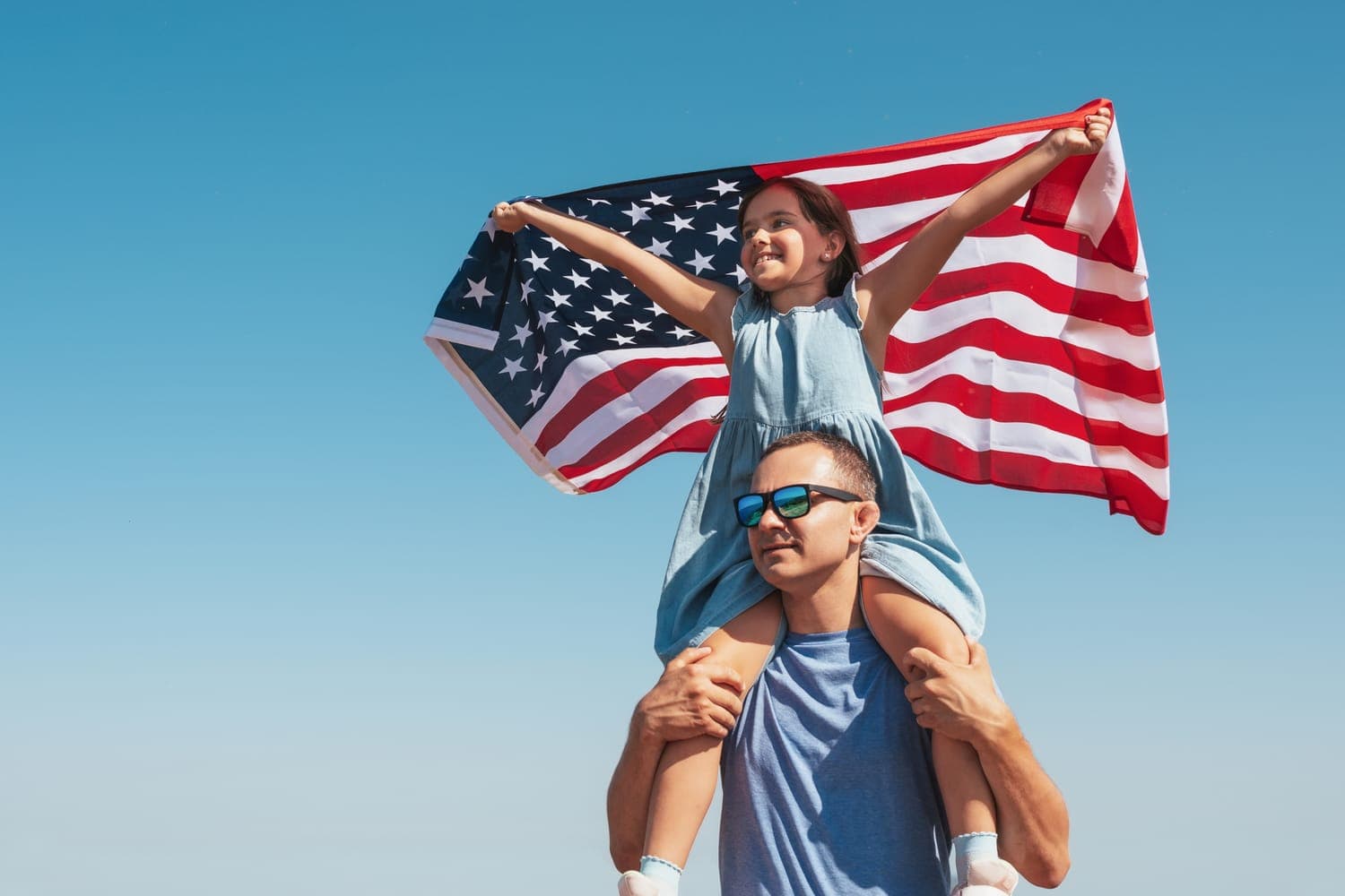 A father carrying his daughter on his shoulders as she holds a US flag